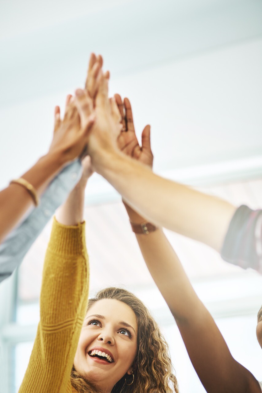 Shot of a group of businesspeople giving each other a high five in an office Freude an der Arbeit